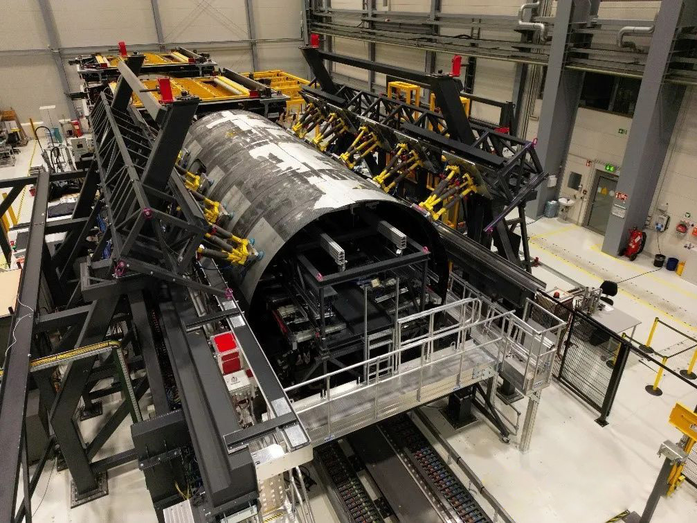 图 5 位于德国施塔德弗劳恩霍夫研究所的MultiFAL平台，正在装配MFFD热塑性复合材料机身壳体。用于夹持固定和高精度调整上机身壳体外形和位置的黄色六足机器人清晰可见。